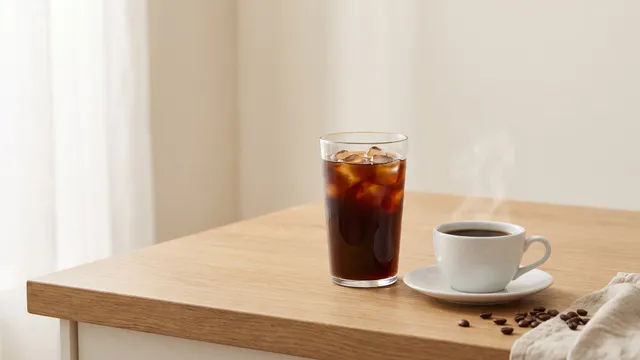 KI-generiertes Symbolbild: hohes Glas Kaffee mit Eis neben einer Tasse mit dampfendem Kaffee auf heller Arbeitsplatte